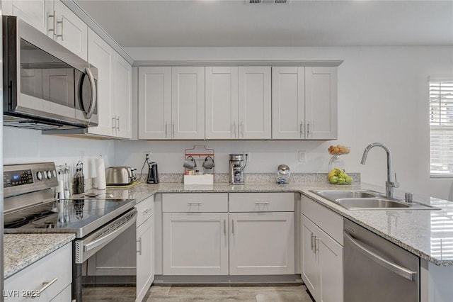 kitchen with visible vents, a sink, a peninsula, light wood-style floors, and stainless steel appliances