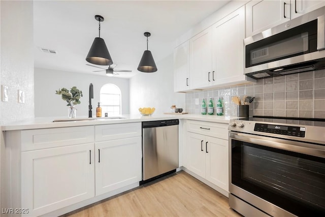 kitchen with decorative backsplash, appliances with stainless steel finishes, a sink, a peninsula, and light wood-style flooring
