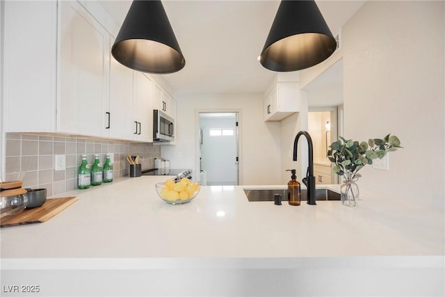 kitchen with a sink, light countertops, white cabinetry, stainless steel microwave, and decorative backsplash