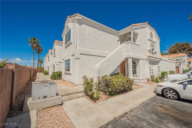 view of side of home featuring fence, uncovered parking, and stucco siding