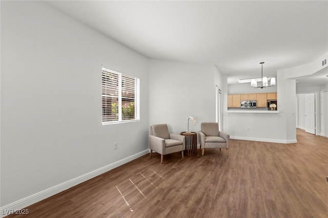 living area featuring a chandelier, wood finished floors, baseboards, and visible vents