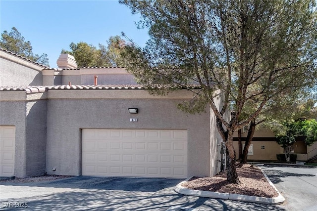 view of property exterior with a chimney, stucco siding, a garage, and a tile roof