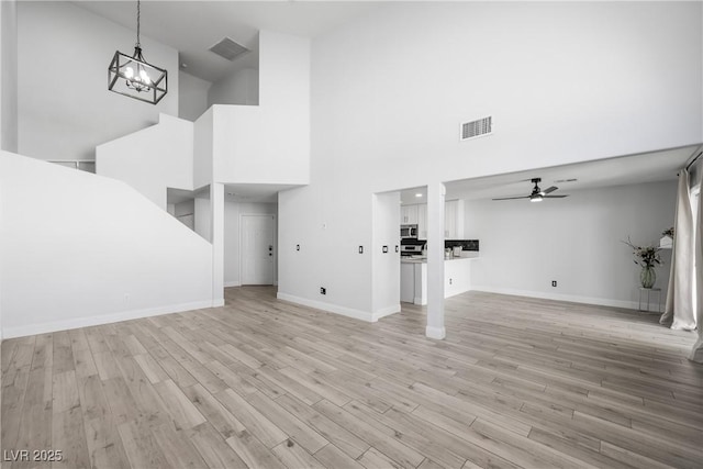 unfurnished living room featuring visible vents, baseboards, a towering ceiling, and ceiling fan with notable chandelier