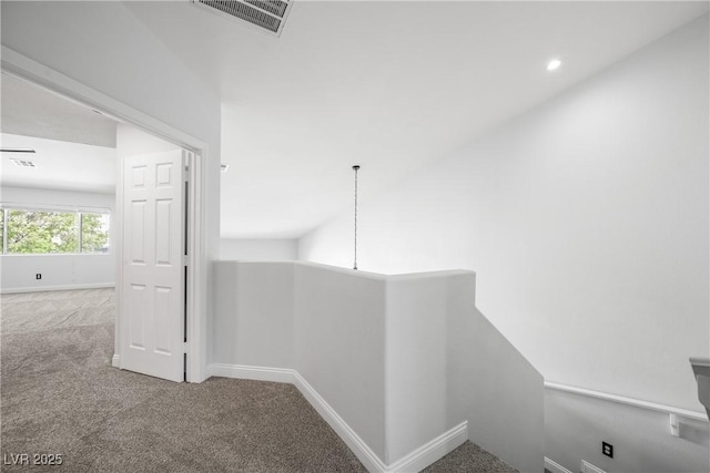 hallway featuring baseboards, visible vents, carpet, and an upstairs landing
