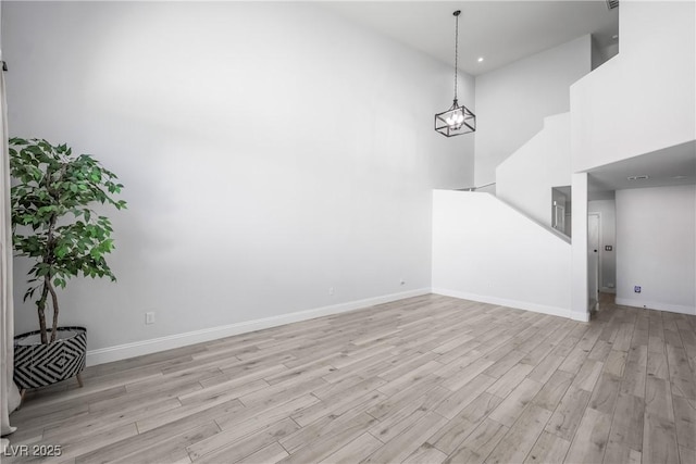unfurnished living room with light wood-style floors, baseboards, a towering ceiling, and a chandelier