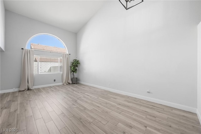 empty room with light wood-style floors, high vaulted ceiling, and baseboards