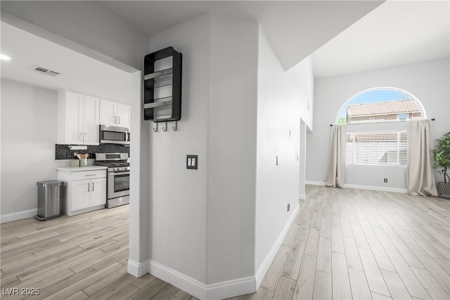 hall featuring baseboards, light wood-type flooring, and visible vents