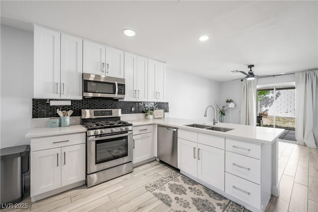 kitchen featuring white cabinets, appliances with stainless steel finishes, a sink, light countertops, and a peninsula