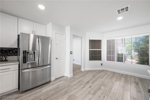 kitchen with stainless steel fridge with ice dispenser, light wood-style floors, white cabinetry, baseboards, and visible vents