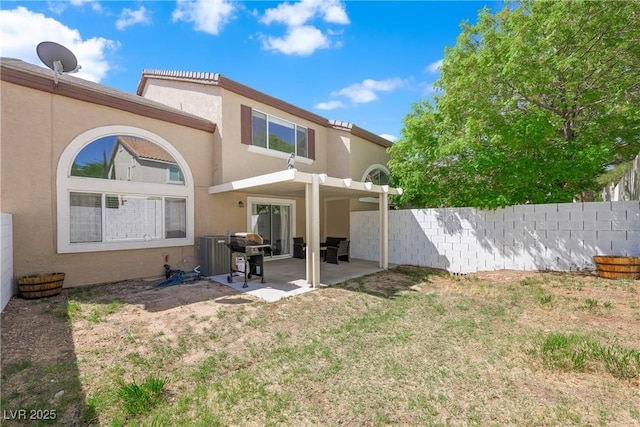 rear view of house featuring a patio, a lawn, fence, and stucco siding