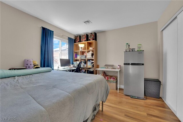 bedroom with freestanding refrigerator, light wood-type flooring, and visible vents