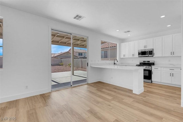8725 Russet Hills Ct, Las Vegas, NV 89147 - kitchen featuring appliances with stainless steel finishes, light countertops, light wood-style flooring, white cabinets, and a peninsula