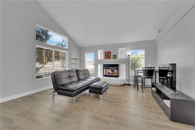 living area with a tiled fireplace, baseboards, high vaulted ceiling, and light wood-type flooring