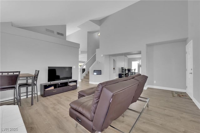 living room featuring visible vents, wood finished floors, baseboards, high vaulted ceiling, and stairway