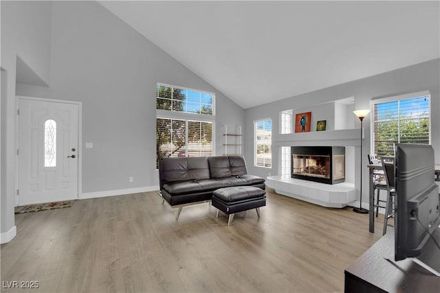 living room with a tiled fireplace, baseboards, wood finished floors, and high vaulted ceiling