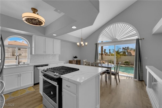 kitchen featuring vaulted ceiling, a sink, white cabinets, a notable chandelier, and stainless steel appliances