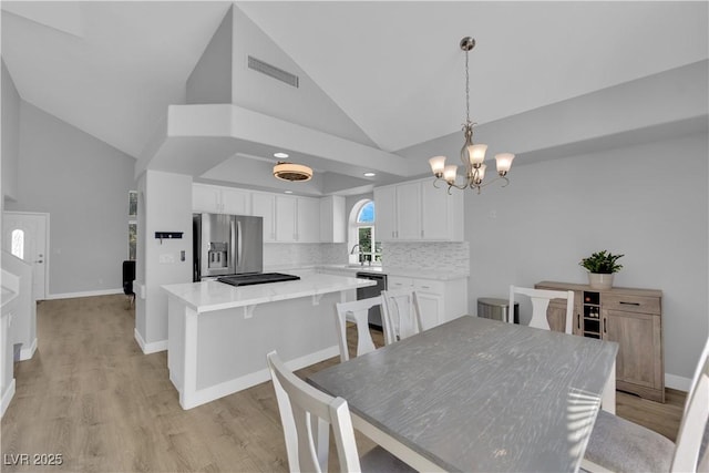 dining room featuring visible vents, light wood-style floors, baseboards, high vaulted ceiling, and a chandelier
