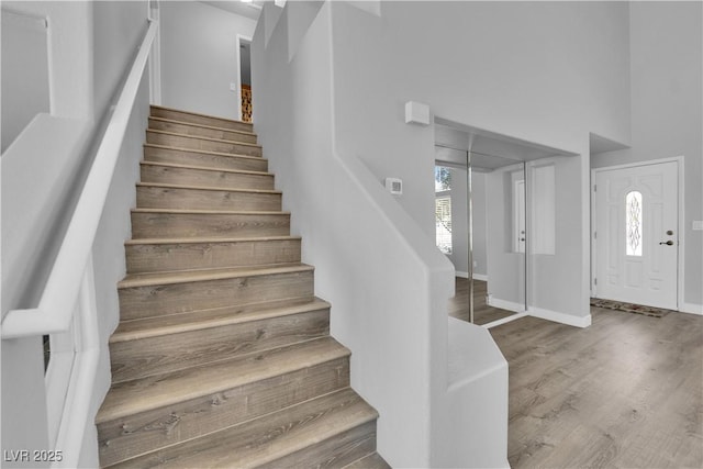 stairway featuring baseboards, a high ceiling, and wood finished floors