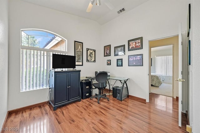 home office featuring visible vents, lofted ceiling, baseboards, a ceiling fan, and light wood-style flooring