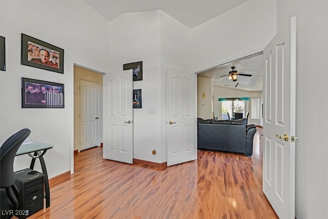 hallway with light wood-style floors, baseboards, and lofted ceiling