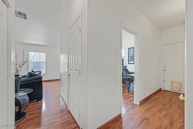 hallway with baseboards, wood finished floors, and visible vents