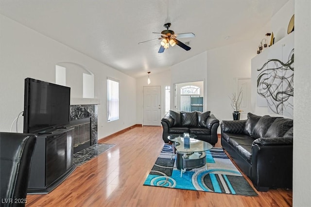 living area with a ceiling fan, a high end fireplace, baseboards, lofted ceiling, and light wood-style flooring