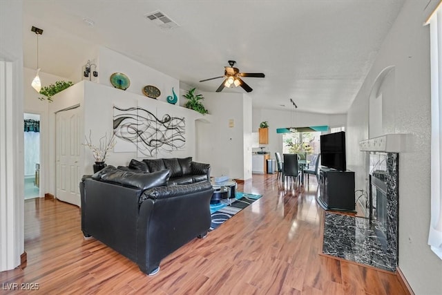 living area featuring ceiling fan, visible vents, a fireplace, vaulted ceiling, and wood finished floors
