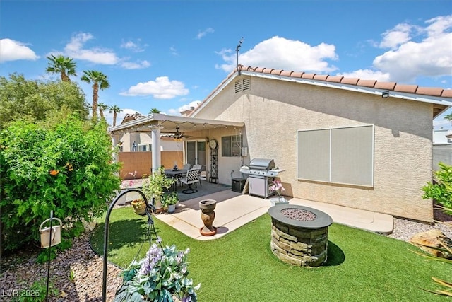 back of property with a patio, stucco siding, a ceiling fan, a lawn, and an outdoor fire pit