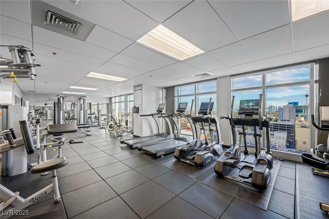 exercise room with a wall of windows, visible vents, a drop ceiling, and a city view