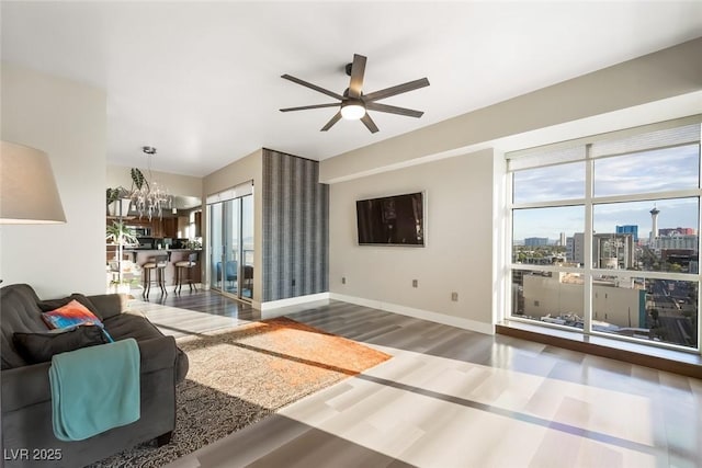 living room featuring baseboards, ceiling fan with notable chandelier, and wood finished floors