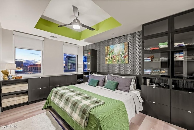 bedroom with visible vents, a ceiling fan, a raised ceiling, and wood finished floors