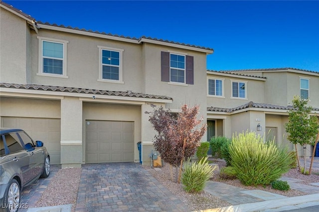multi unit property featuring decorative driveway, an attached garage, a tile roof, and stucco siding