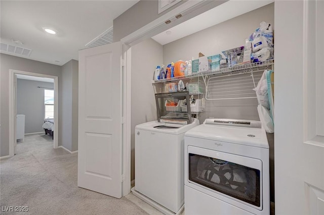 clothes washing area featuring laundry area, visible vents, light carpet, baseboards, and washer and clothes dryer
