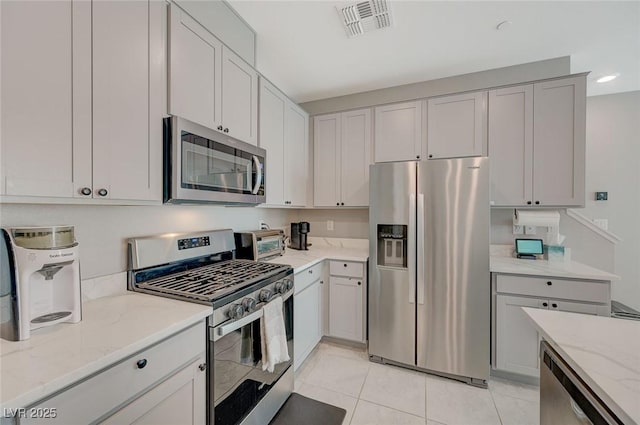 kitchen with visible vents, a toaster, light stone countertops, appliances with stainless steel finishes, and light tile patterned floors