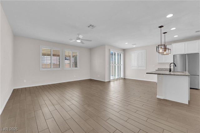 unfurnished living room featuring a healthy amount of sunlight, baseboards, ceiling fan, and visible vents