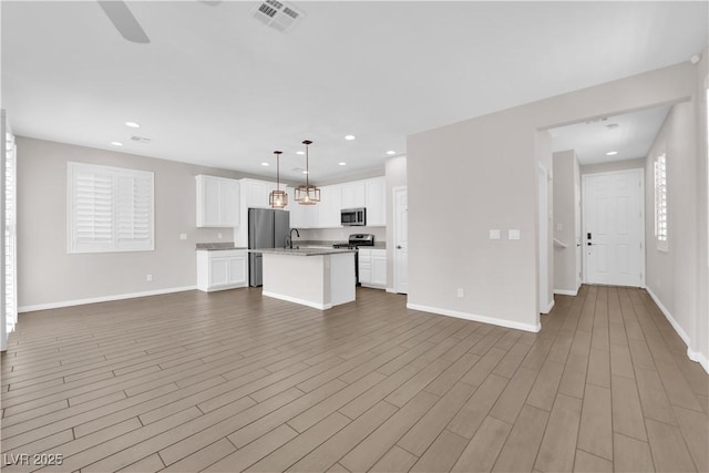 kitchen with visible vents, a kitchen island with sink, open floor plan, white cabinetry, and appliances with stainless steel finishes