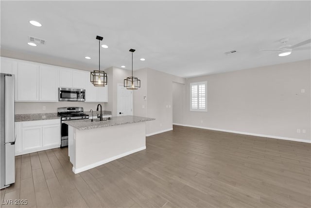 kitchen with appliances with stainless steel finishes, a sink, a kitchen island with sink, wood finished floors, and visible vents
