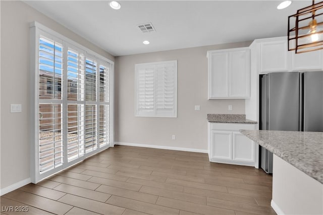 kitchen featuring freestanding refrigerator, white cabinetry, baseboards, and visible vents