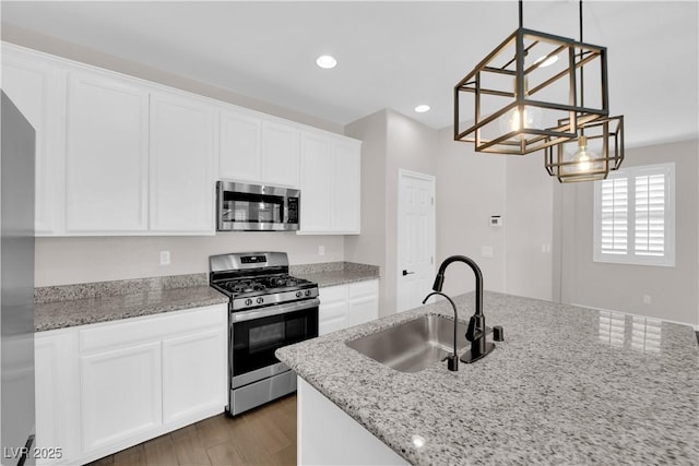 kitchen featuring white cabinets, appliances with stainless steel finishes, light stone counters, a sink, and a chandelier