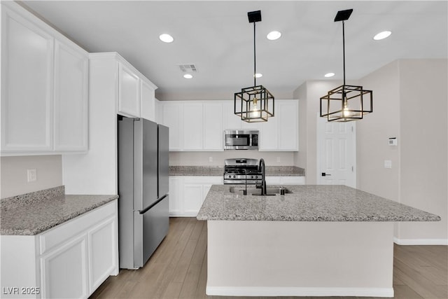 kitchen with visible vents, a center island with sink, a sink, light wood-style floors, and stainless steel appliances