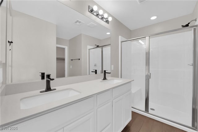 bathroom featuring wood finished floors, a sink, a stall shower, and double vanity
