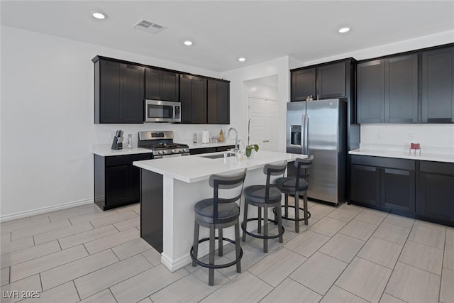 kitchen with a kitchen bar, visible vents, appliances with stainless steel finishes, a sink, and light countertops