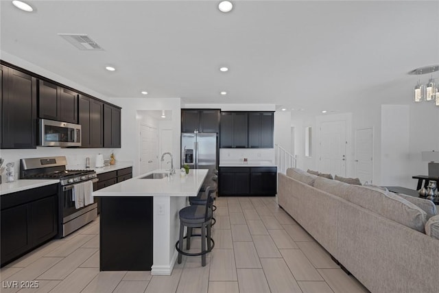 kitchen with open floor plan, a breakfast bar area, light countertops, a sink, and appliances with stainless steel finishes
