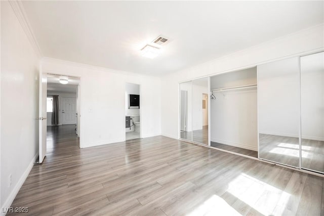 unfurnished bedroom with visible vents, crown molding, wood finished floors, baseboards, and a closet