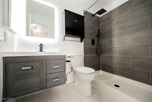 bathroom with toilet, a tile shower, and vanity