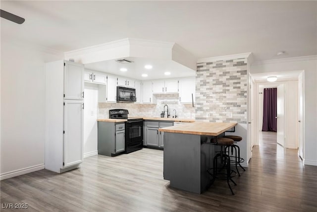 kitchen featuring crown molding, a kitchen breakfast bar, tasteful backsplash, wood counters, and black appliances