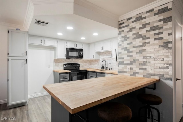 kitchen featuring visible vents, crown molding, a sink, black appliances, and butcher block counters