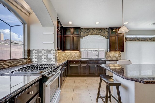 kitchen with light tile patterned flooring, appliances with stainless steel finishes, a sink, dark stone countertops, and glass insert cabinets