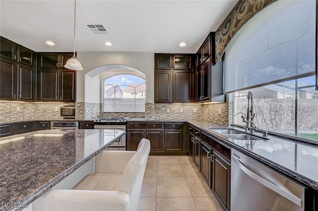 kitchen featuring a sink, arched walkways, dark stone counters, stainless steel appliances, and visible vents
