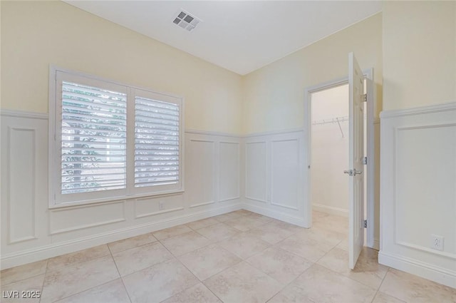 unfurnished room with wainscoting, a decorative wall, light tile patterned flooring, and visible vents